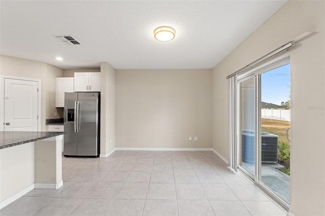 kitchen featuring light tile patterned floors, white cabinetry, stainless steel refrigerator with ice dispenser, a textured ceiling, and dark stone counters