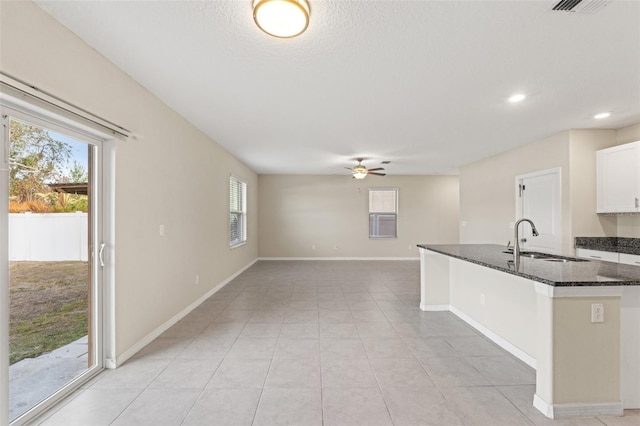 kitchen featuring sink, white cabinetry, light tile patterned floors, dark stone countertops, and ceiling fan