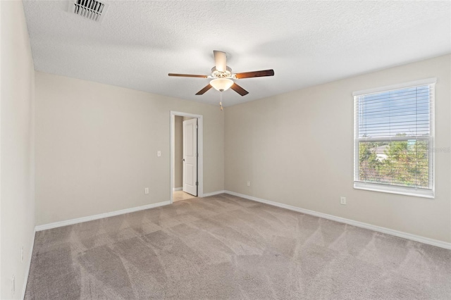 spare room featuring ceiling fan, light carpet, and a textured ceiling