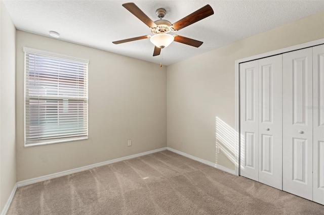 unfurnished bedroom featuring ceiling fan, light colored carpet, a textured ceiling, and a closet