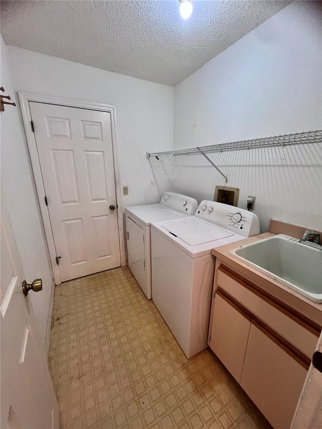 clothes washing area featuring cabinets, sink, washer and dryer, and a textured ceiling