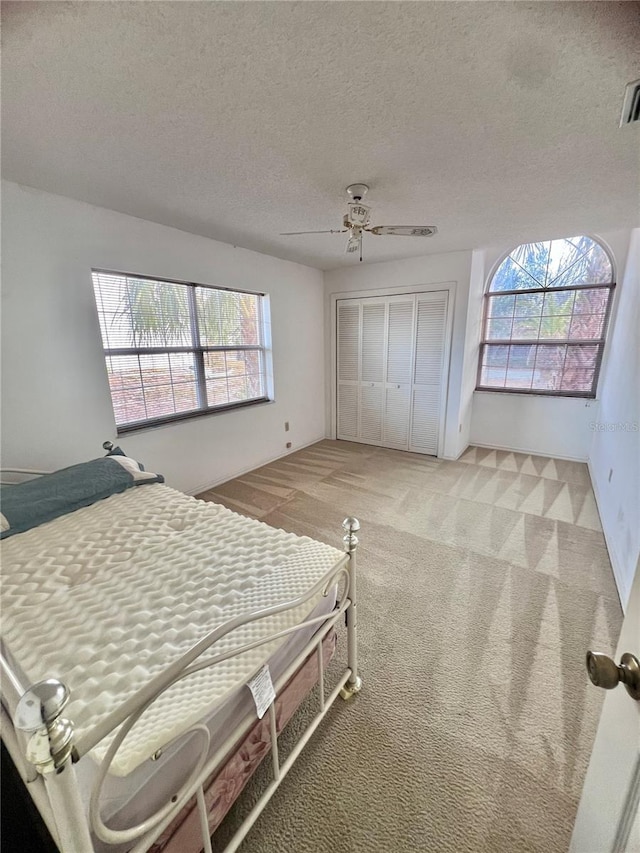 carpeted bedroom with ceiling fan, a closet, and a textured ceiling