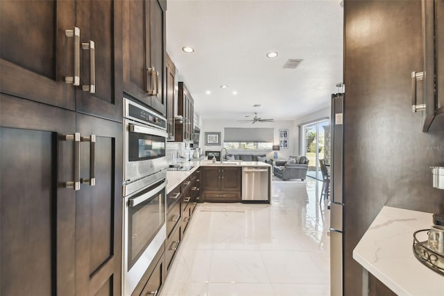 kitchen featuring stainless steel appliances, light stone countertops, dark brown cabinetry, and ceiling fan