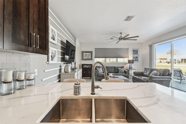 kitchen with light stone counters, sink, dark brown cabinetry, and ceiling fan