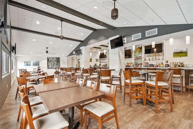 dining area featuring bar, lofted ceiling with beams, light hardwood / wood-style floors, and a paneled ceiling