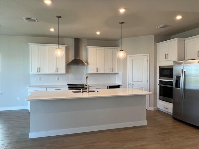 kitchen with a center island with sink, decorative backsplash, appliances with stainless steel finishes, a sink, and wall chimney exhaust hood