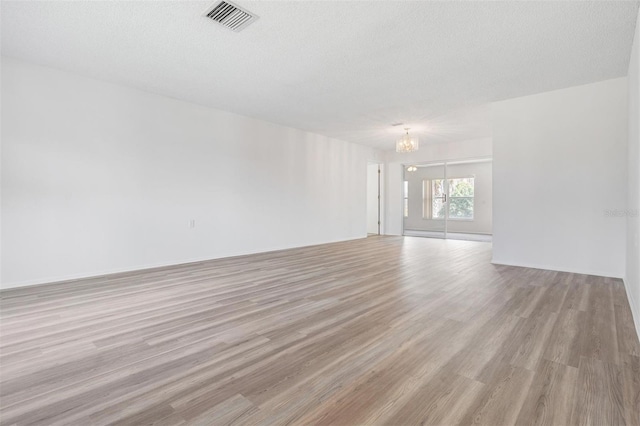 unfurnished room featuring a notable chandelier, light hardwood / wood-style flooring, and a textured ceiling