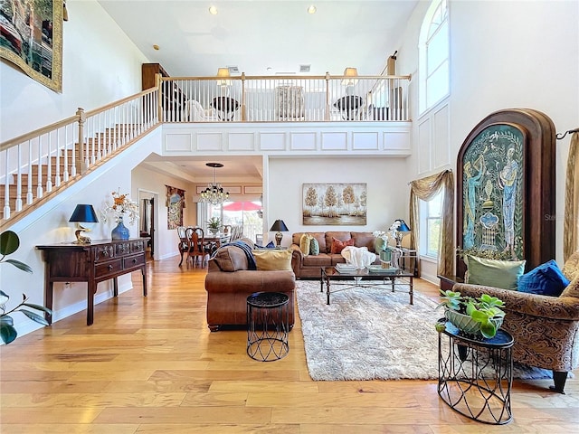 living room with an inviting chandelier, a towering ceiling, and light wood-type flooring