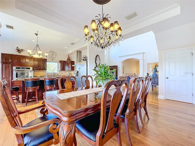 dining room featuring a notable chandelier, a tray ceiling, light hardwood / wood-style flooring, and ornamental molding