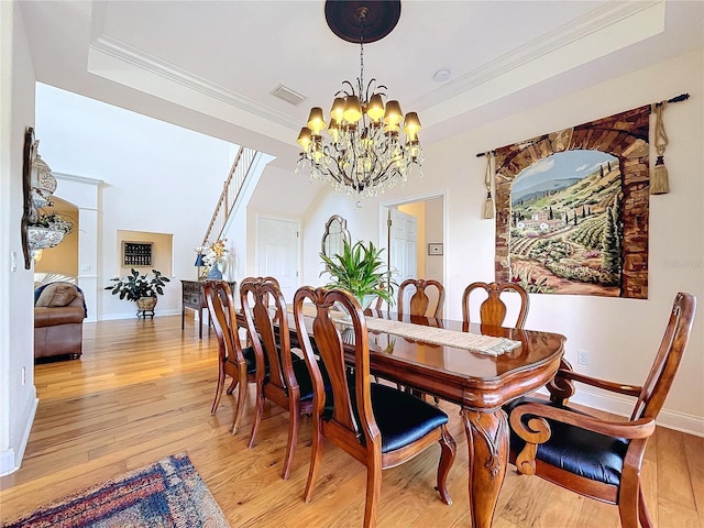 dining area with a notable chandelier, crown molding, light hardwood / wood-style floors, and a raised ceiling