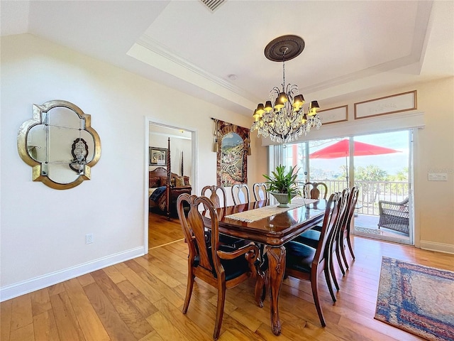 dining area featuring a raised ceiling, crown molding, a chandelier, and light hardwood / wood-style flooring