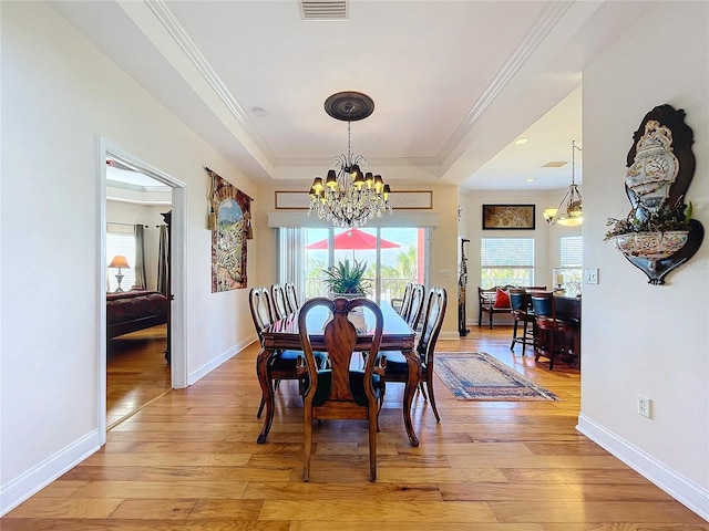 dining room featuring an inviting chandelier, a tray ceiling, ornamental molding, and light wood-type flooring