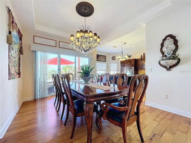 dining area with ornamental molding, light hardwood / wood-style flooring, an inviting chandelier, and a tray ceiling