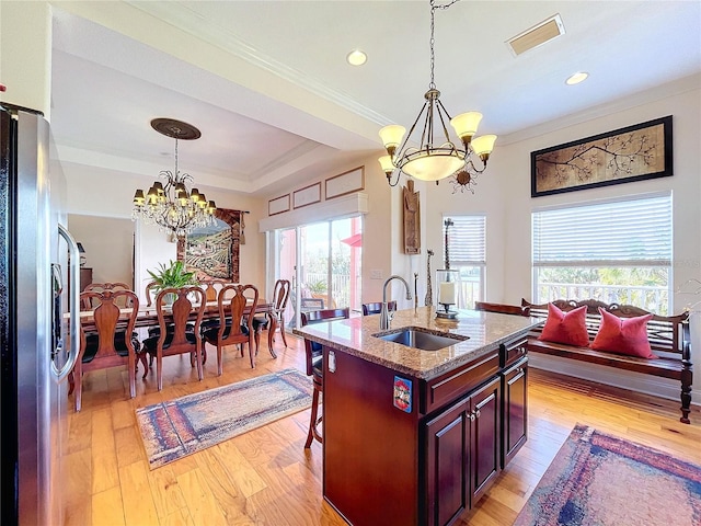 kitchen with sink, a chandelier, stainless steel fridge with ice dispenser, a center island with sink, and a raised ceiling