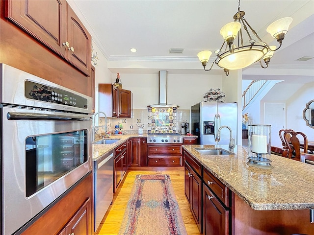 kitchen with wall chimney exhaust hood, stainless steel appliances, sink, and a center island with sink