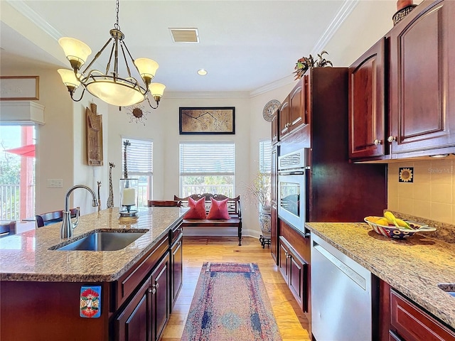 kitchen with sink, appliances with stainless steel finishes, a kitchen island with sink, hanging light fixtures, and ornamental molding