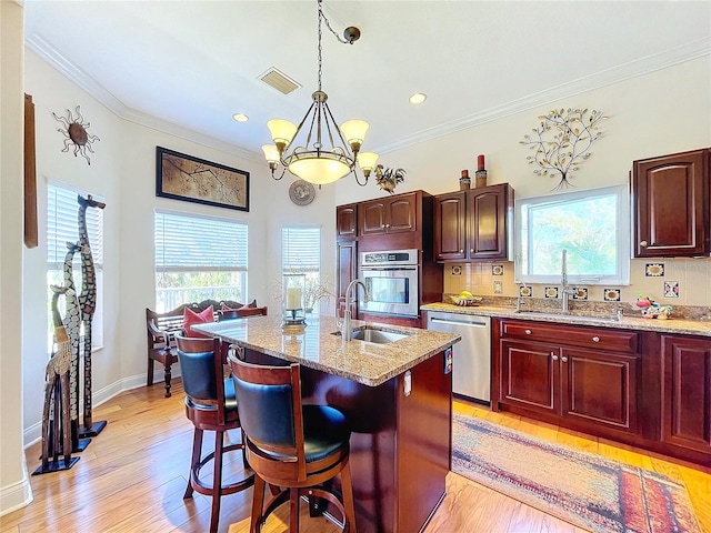 kitchen with appliances with stainless steel finishes, sink, hanging light fixtures, a kitchen island with sink, and light stone countertops