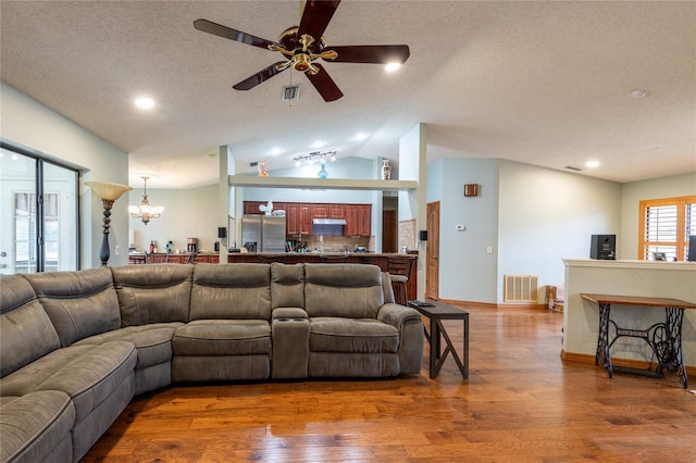 living room with ceiling fan with notable chandelier, lofted ceiling, and hardwood / wood-style floors