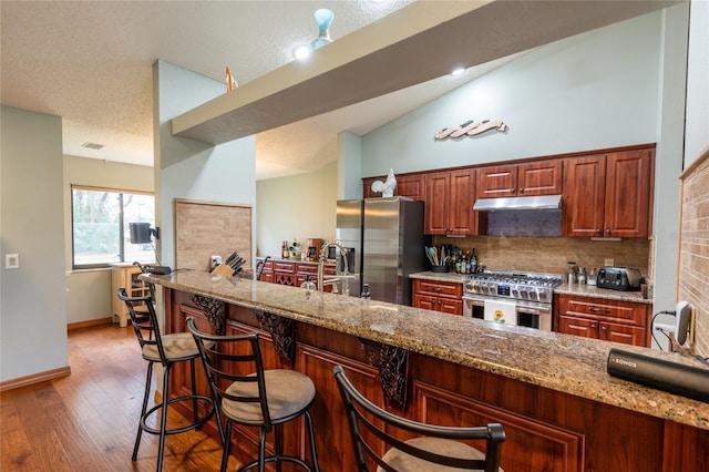 kitchen featuring a breakfast bar, dark hardwood / wood-style flooring, decorative backsplash, stainless steel appliances, and light stone countertops