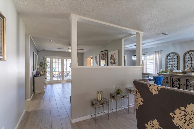 hall featuring french doors, decorative columns, a textured ceiling, and light wood-type flooring