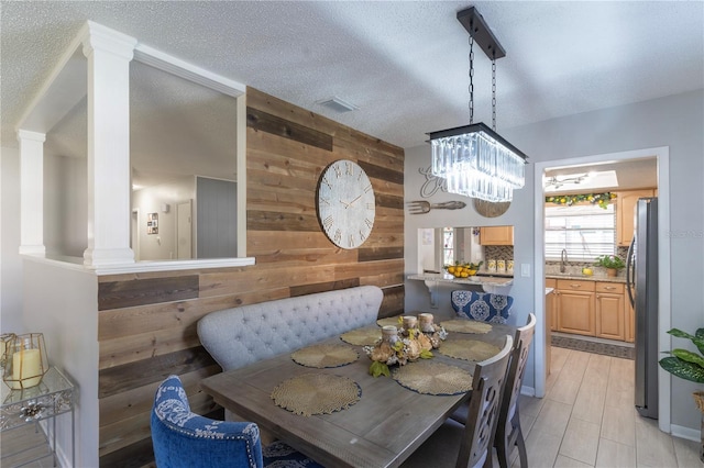 dining room with sink, a textured ceiling, breakfast area, a chandelier, and wood walls