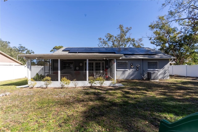 rear view of property with central AC unit, a yard, a sunroom, and solar panels