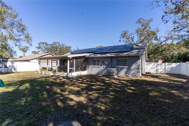 back of house featuring a lawn, a trampoline, central AC unit, a sunroom, and solar panels