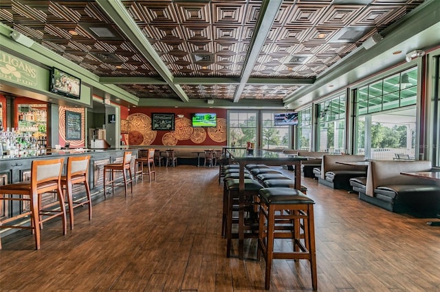 dining room featuring beamed ceiling, indoor bar, wood-type flooring, and coffered ceiling