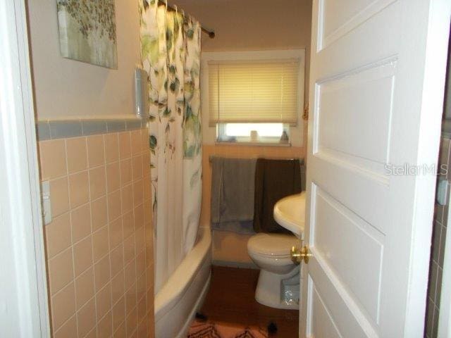 bathroom featuring shower / bath combination with curtain, toilet, and tile walls