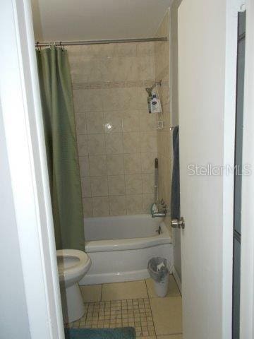 bathroom with shower / bathtub combination with curtain, tile patterned floors, and toilet