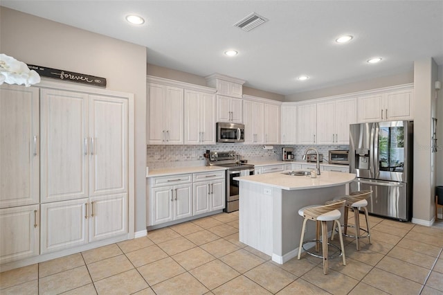 kitchen featuring stainless steel appliances, an island with sink, white cabinets, and a kitchen bar