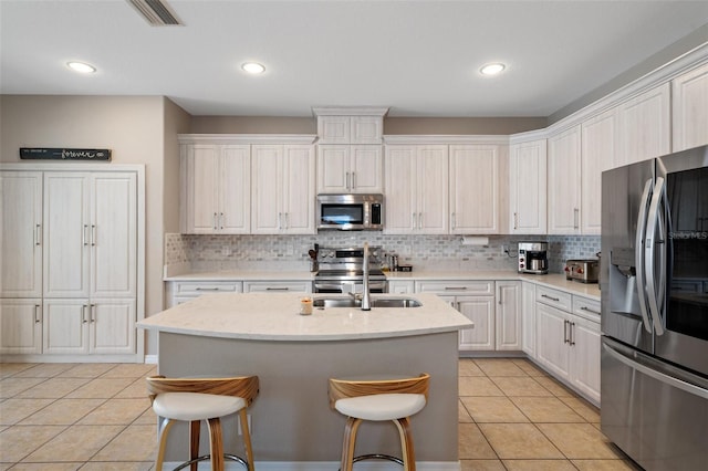 kitchen with appliances with stainless steel finishes, an island with sink, sink, white cabinets, and light tile patterned floors