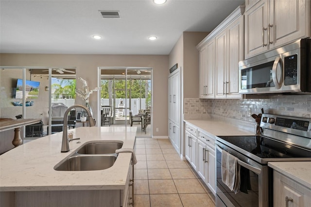 kitchen with appliances with stainless steel finishes, sink, a kitchen island with sink, and decorative backsplash