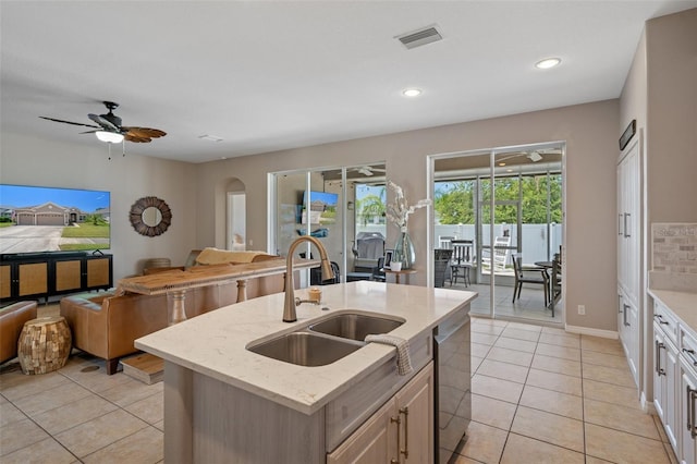 kitchen with an island with sink, sink, stainless steel dishwasher, light tile patterned floors, and light stone counters