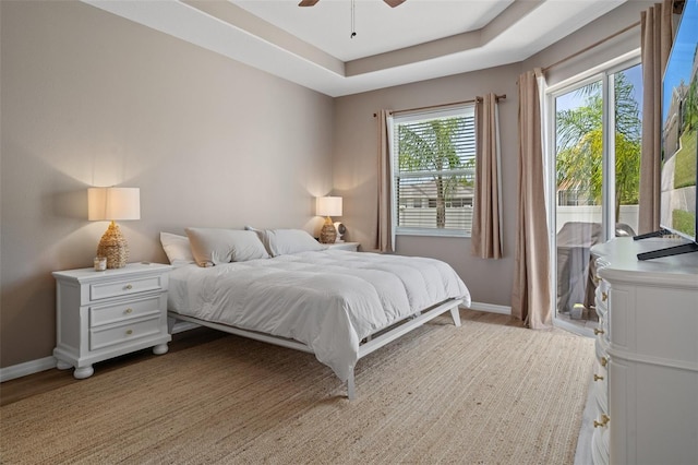 bedroom featuring ceiling fan, access to outside, light wood-type flooring, and a tray ceiling