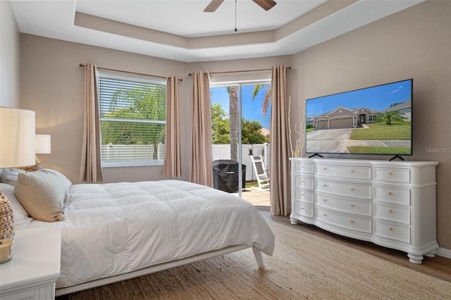 bedroom featuring ceiling fan, a raised ceiling, hardwood / wood-style floors, and access to outside