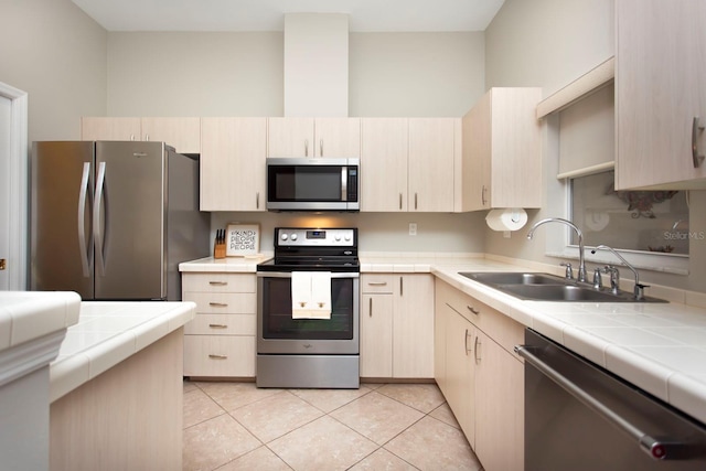 kitchen with sink, stainless steel appliances, light tile patterned flooring, light brown cabinetry, and tile countertops