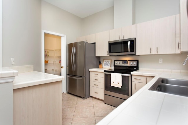 kitchen featuring sink, tile countertops, light tile patterned flooring, and appliances with stainless steel finishes