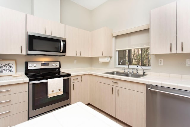 kitchen with stainless steel appliances, tile counters, light brown cabinetry, and sink