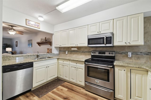 kitchen with light stone counters, sink, stainless steel appliances, and light hardwood / wood-style floors