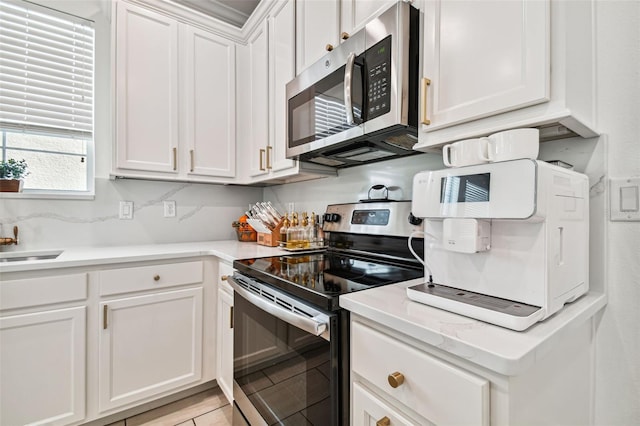 kitchen with stainless steel appliances, sink, light tile patterned floors, and white cabinets