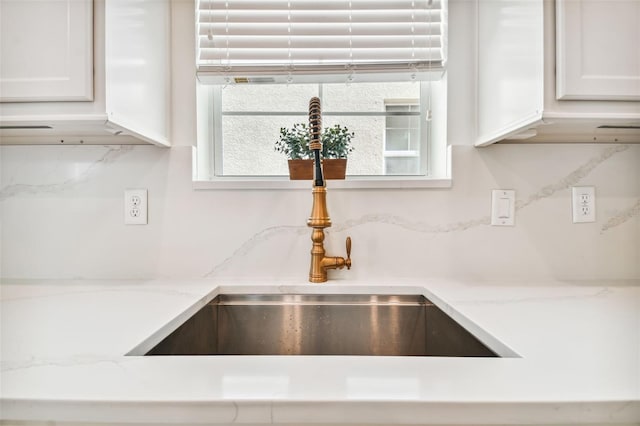 interior details with white cabinetry, light stone countertops, sink, and tasteful backsplash