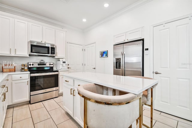 kitchen featuring ornamental molding, stainless steel appliances, a breakfast bar area, and white cabinets