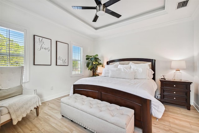 bedroom featuring ornamental molding, light hardwood / wood-style floors, ceiling fan, and a tray ceiling