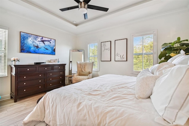 bedroom with crown molding, light hardwood / wood-style flooring, ceiling fan, and a tray ceiling