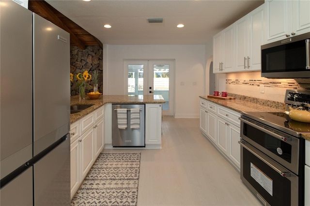 kitchen featuring stone counters, white cabinetry, appliances with stainless steel finishes, and kitchen peninsula