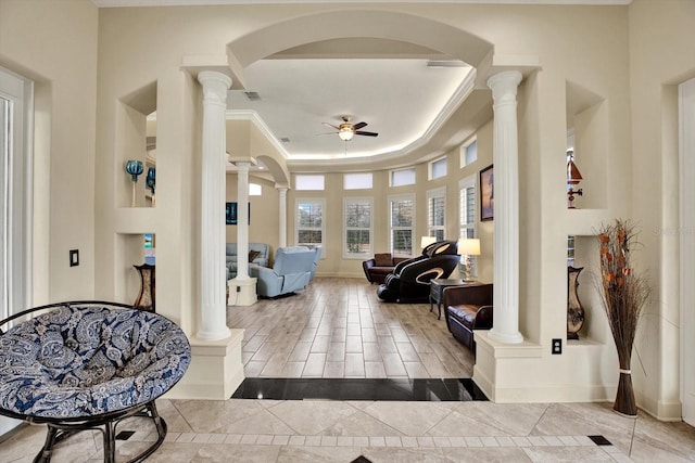 entrance foyer featuring ornate columns, ornamental molding, ceiling fan, and a tray ceiling