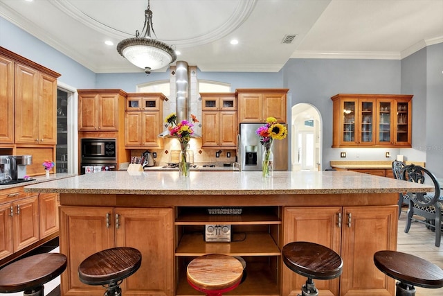 kitchen with stainless steel fridge, black microwave, wall oven, an island with sink, and wall chimney exhaust hood