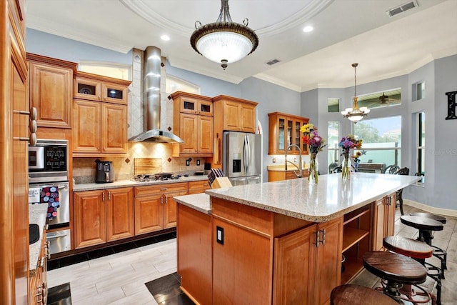 kitchen featuring tasteful backsplash, an island with sink, pendant lighting, stainless steel appliances, and wall chimney range hood