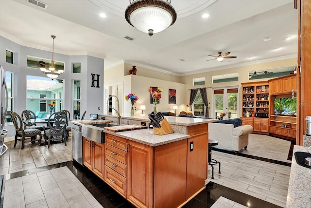 kitchen with sink, dishwasher, pendant lighting, light stone countertops, and a kitchen island with sink